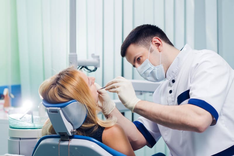 Dentist examining a patient’s teeth while the patient sits in a dental chair