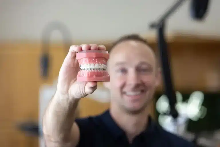 Orthodontist holding a dental model with braces, demonstrating how braces can correct tooth alignment and bite problems.